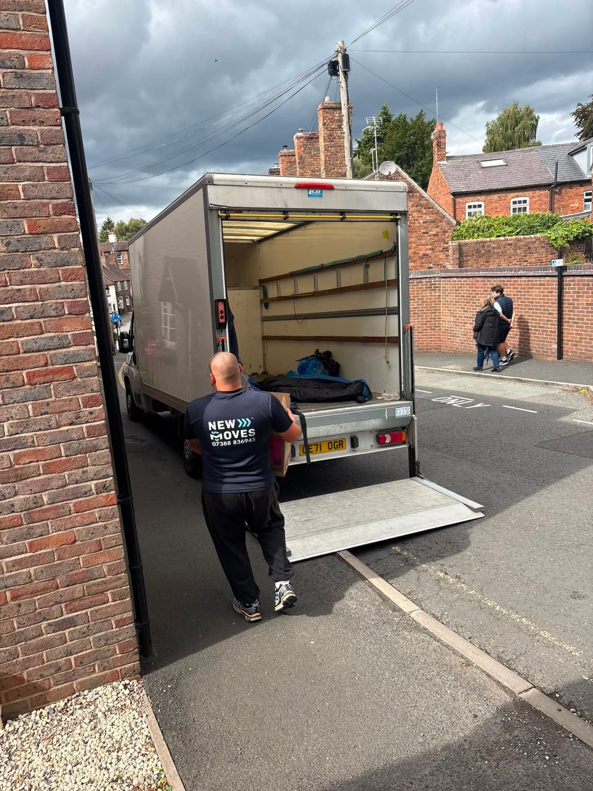 A New Moves Removals team member loading a labelled box into the van on a narrow street