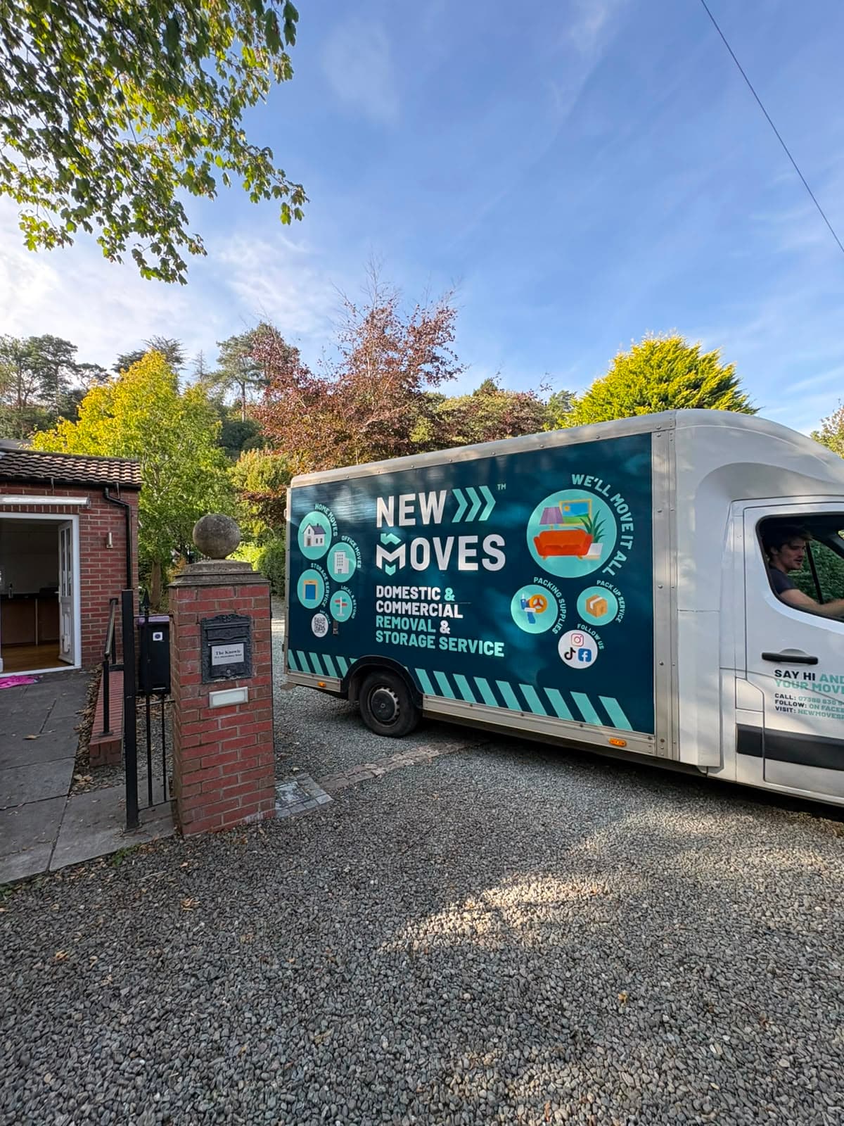 A New Moves Removals van parked on a gravel driveway beside a stone gate pillar