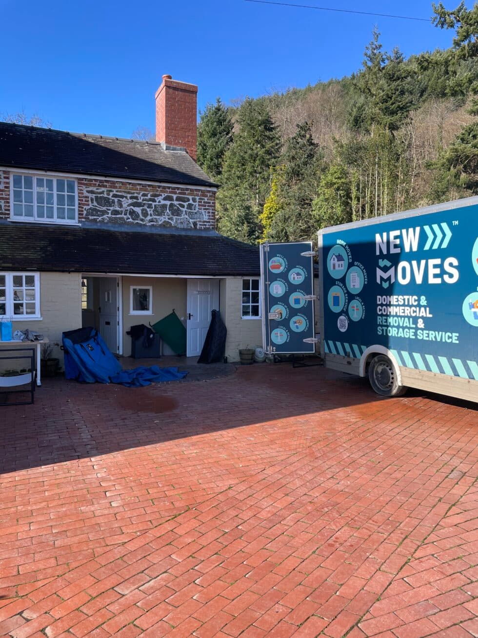 A New Moves Removals van backed up to the front door of a stone cottage, with wrapped furniture ready to load