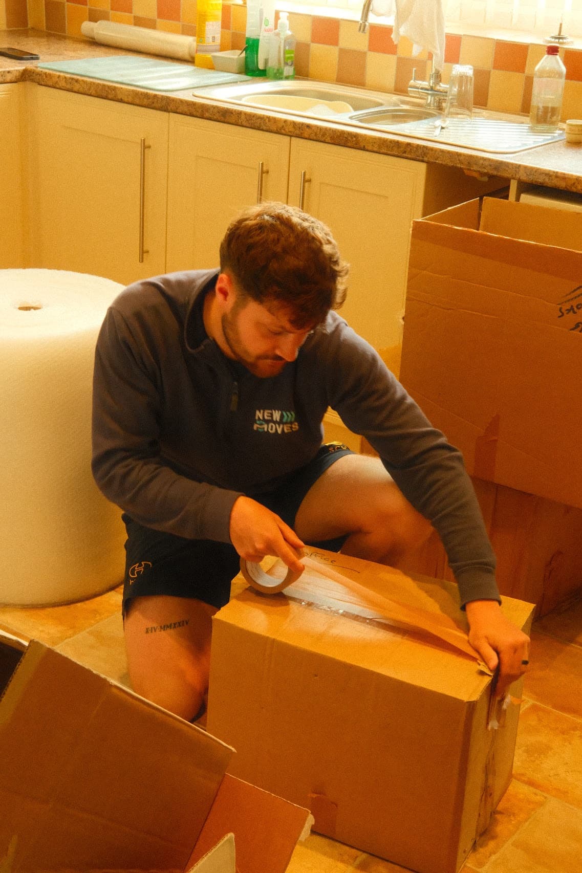 A New Moves Removals team member sealing a moving box in a customer's kitchen