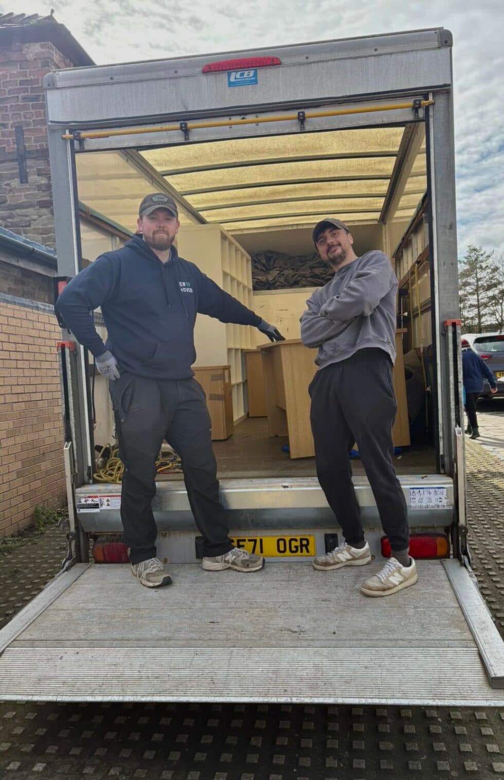 Two New Moves Removals team members standing in the back of a removal van loaded with office desks and furniture