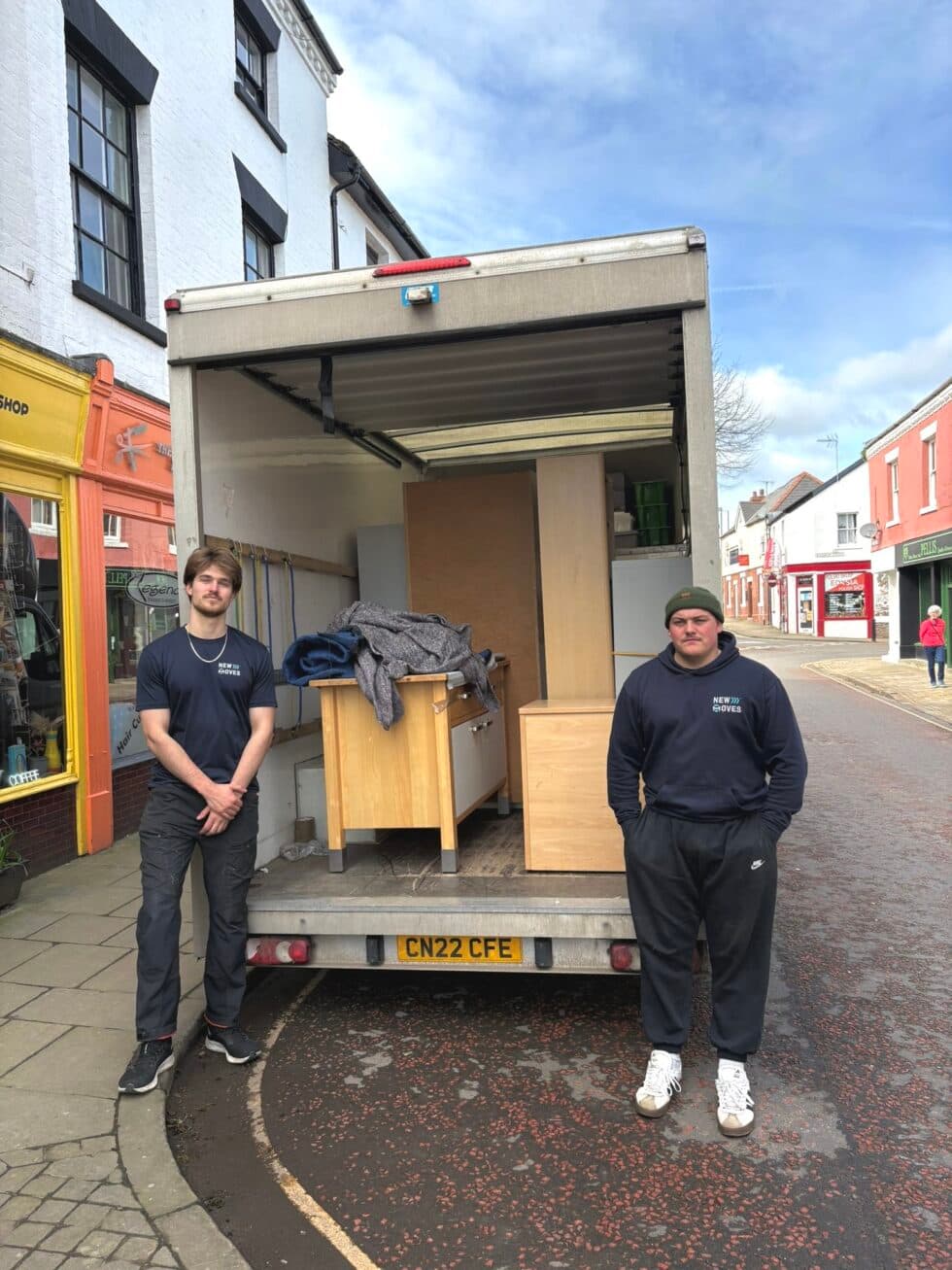 Two New Moves Removals team members standing beside an open removal van loaded with office furniture and equipment