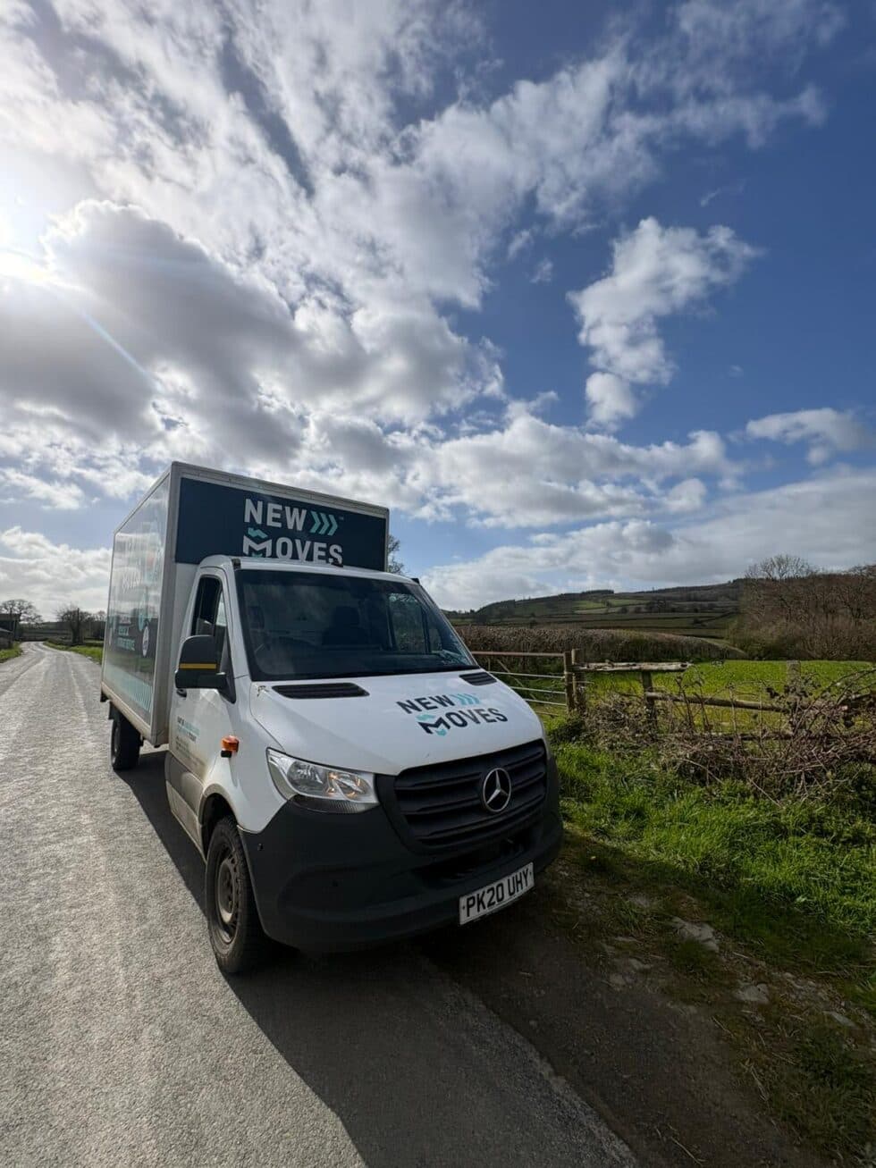New Moves Removals branded van parked on a countryside road under a partly cloudy sky
