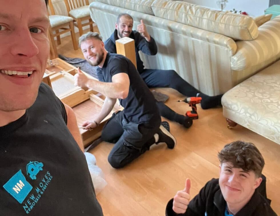 New Moves Removals team members smiling and giving thumbs up while dismantling furniture during a packing job